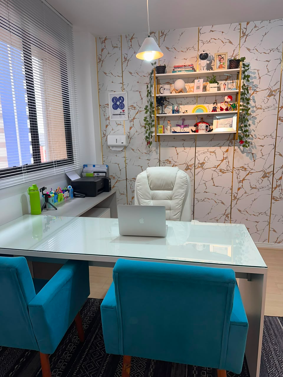 Consultório de fonoaudiologia com mesa de vidro e prateleiras decoradas
